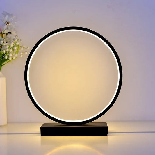 Moderne Luce dell'Anello Nachttischlampe mit kreisförmigem LED-Licht und minimalistischem Design auf einem Nachttisch.