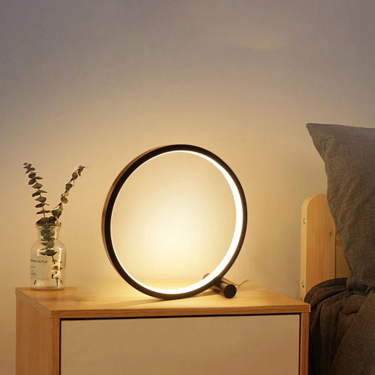 Eine stilvolle 'CircoloLuce' Nachttischlampe in minimalistischem Design leuchtet auf einem Nachttisch, neben einer Vase mit Zweigen.